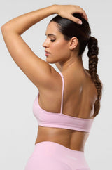 Woman wearing a pink sports bra and leggings on a light gray background