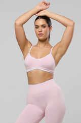A woman modeling a light pink activewear set consisting of a sports bra and high-waisted leggings, paired with white socks and white sneakers, against a solid light gray background.