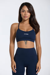Woman wearing a navy sports bra and leggings with 'LESS DRAMA' text on a white background