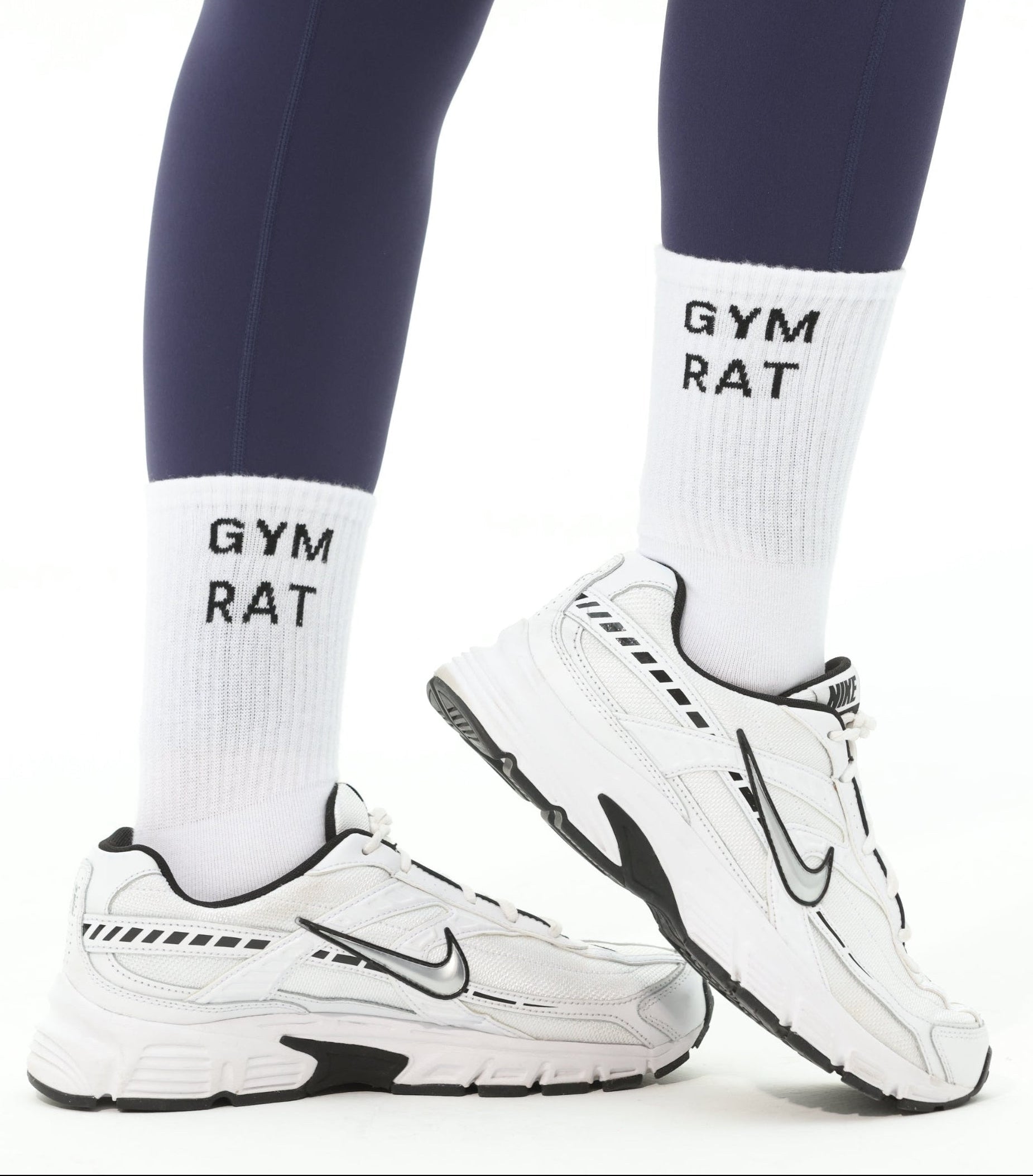 Person wearing navy leggings and white sneakers with 'Gym Rat' socks on a white background