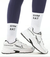 Person wearing navy leggings and white sneakers with 'Gym Rat' socks on a white background