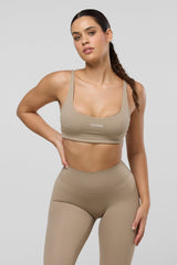 Woman wearing a beige sports bra and leggings set on a plain background
