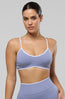 A woman modeling a matching light periwinkle blue activewear set consisting of a sports bra and high-waisted leggings, styled with white socks and gray sneakers against a solid gray studio background.