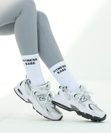 Person wearing white athletic shoes and gray leggings with 'Fitness Babe' text on a white background
